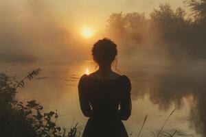 A woman standing in front of a river at sunset photo