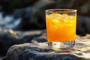A glass of orange juice sitting on a rock photo