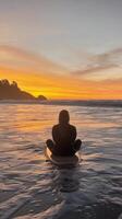 A person sitting on a surfboard at sunset photo