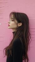 A woman with long hair standing in front of a pink wall photo