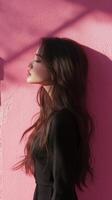 A woman with long hair standing against a pink wall photo