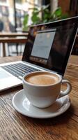 A cup of coffee and a laptop on a wooden table photo