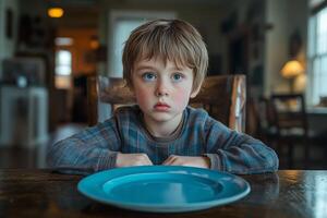 A young boy sits at a table with a plate photo
