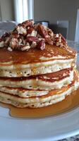 A stack of pancakes topped with pecans and syrup photo