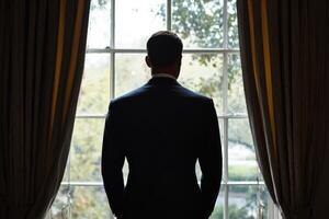 A man in a suit stands in front of a window photo