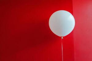 A white balloon is hanging from a red wall photo