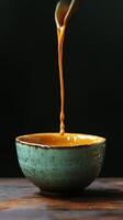 A spoon is pouring syrup into a bowl of orange liquid photo