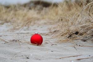 A red christmas ball sits in the sand photo