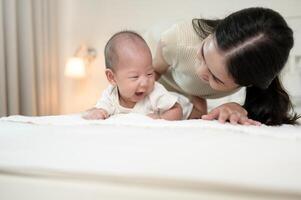 Mother Encourages Her Baby to Crawl on a Soft Bed in a Cozy Room During Afternoon Playtime photo