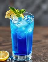 Refreshing blue cocktail garnished with lemon and mint served in a clear glass photo