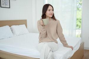 Young Woman Enjoying a Cup of Tea While Sitting on a Bed in a Bright, Airy Room photo