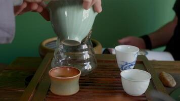 Cropped image of man preparing traditional herbal Chinese tea. Ceramic containers on wooden tray. He is sitting with friend at home. video