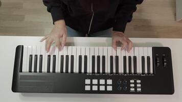 Midsection of woman playing keyboard on white table. Female artist is enjoying rhythm on instrument. She is sitting at studio. Top to down view overhead video