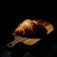A croissant on a wooden board in the dark photo