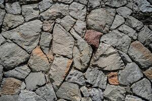 A stone wall with a few large stones and a small one. The wall is made of gray and brown stones photo