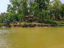 a house on the bank of a river with trees in the background photo