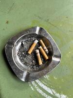 a cigarette in a metal ashtray on a green surface photo