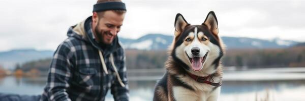 Happy man playing with his husky dog by the lake during a cloudy day in the mountains photo