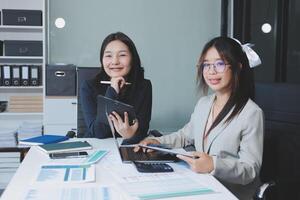 Two asian women sitting at a desk with a tablet photo