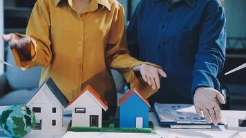 Two people are holding a model of a house and a wind turbine video