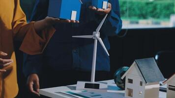A woman holding a model house and a wind turbine video