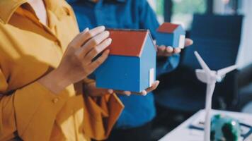 Two people holding a house model in front of a wind turbine video
