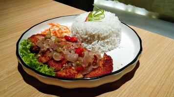 a plate of rice and chicken katsu with sambal matah and fresh vegetables on a wooden table photo