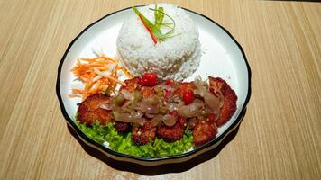 A plate of rice and chicken katsu with sambal matah and fresh vegetables on a wooden table, 45 degrees angle shoot photo