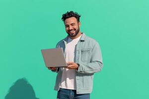 Happy man enjoying technology while smiling and holding a laptop against a calm light blue background photo