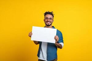 Happy man joyfully showcases a blank board against a vibrant yellow backdrop in a lively indoor setting photo