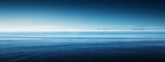 Expansive horizon meeting the tranquil depths of a serene blue ocean under a clear sky at dawn photo