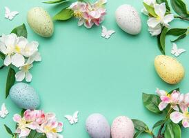 Easter eggs and spring flowers creating a frame on a turquoise background photo