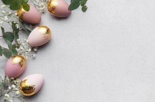 Elegant easter eggs with gold leaf and eucalyptus leaves creating a border on gray background photo