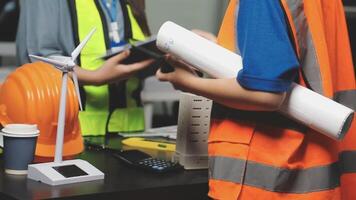 Two people in safety vests and hard hats holding papers and a wind turbine video