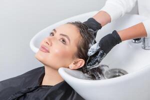 The stylist, wearing a sleek uniform, carefully massages shampoo into the woman's scalp photo