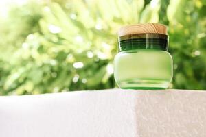 A close-up of a jar of cream made of green glass with a wooden lid. A mock-up of a cosmetics against a background of fresh foliage. The layout of the bottle and trees. photo