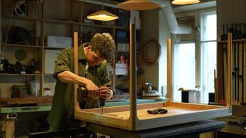 Carpenter screws table frame to tabletop with screwdriver. Final stage of installation. video