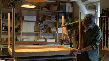 Carpenter screws table frame to tabletop with screwdriver. Final stage of installation. video
