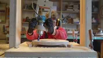 Man carpenter in noise-cancelling headphone, glasses, respirator drilling wooden plank in joinery video