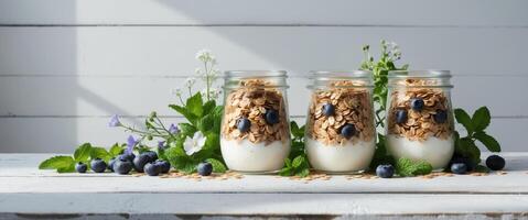 Nutritious oat granola and yogurt in glass jars arranged in a row on a white wooden table with toppings and herbs for a fresh and healthy display. photo