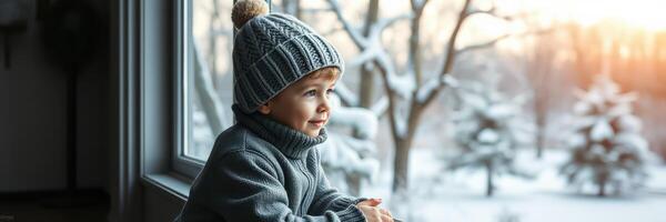 Child in cozy winter attire gazing out at snowy landscape during golden hour in a warm indoor setting photo