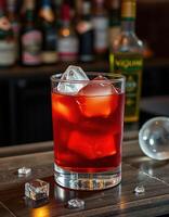 Refreshing cocktail served in a clear glass with ice cubes against a blurred background of bottles in a dimly lit bar photo