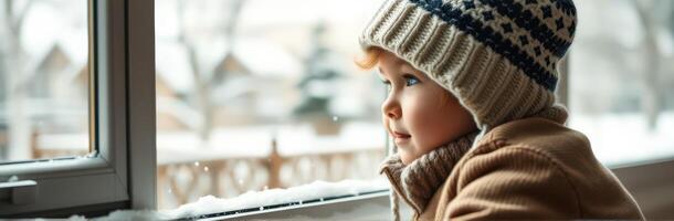 Child gazing out the window on a snowy winter day while wearing a warm hat and coat photo