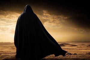 man dressed in dark blue jubba and taqiyah cap stands in open desert. wind flows softly lifting fabric of his robe against dramatic evening sky photo