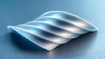 Close-up of a textured, wave-shaped metallic object reflecting light on a smooth surface photo