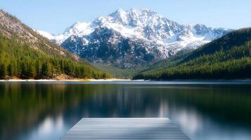 A dock in front of a mountain lake with snow capped mountains in the background photo