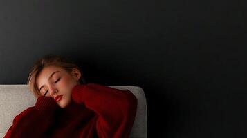 Young woman in cozy sweater resting on a sofa against a dark wall, creating a tranquil atmosphere photo