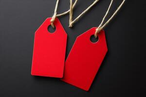 Two red blank price tags hanging on string against black background photo
