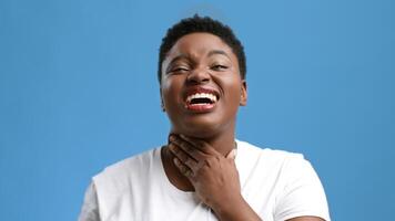 A young African American woman shows a pained expression while touching her neck in a studio setting. The bright blue background contrasts with her chubby features and emotional display. video