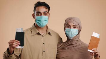 A married Arab couple, both wearing masks, smiles at each other while holding documents in a studio with a warm background. Their expressions convey love and excitement during this moment. video